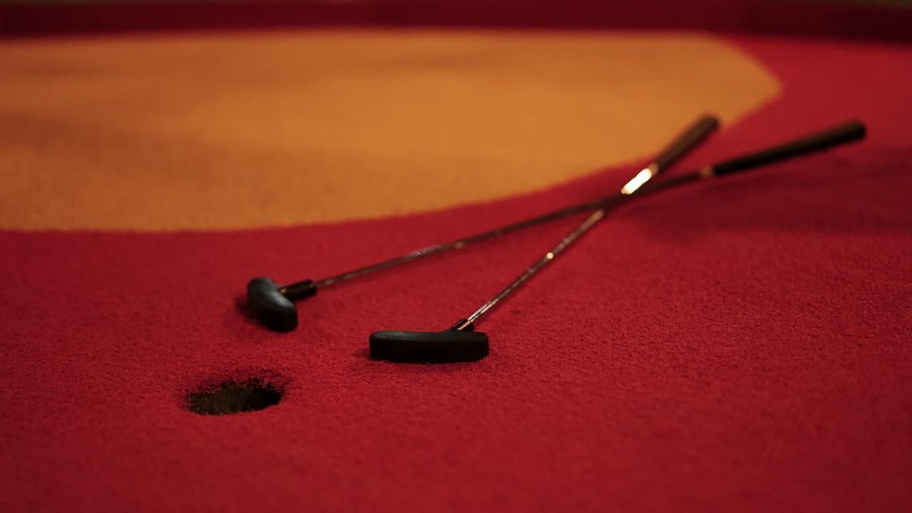 A red golf ball narrowly misses the hole on a miniature golf course. Warm lighting enhances the vibrant red and orange colors