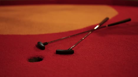 A red golf ball narrowly misses the hole on a miniature golf course. Warm lighting enhances the vibrant red and orange colors