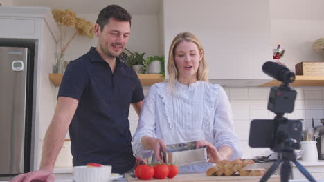 pareja vlogging haciendo video de redes sociales sobre la comida en casa en la cocina en el teléfono móvil - filmado en cámara lenta