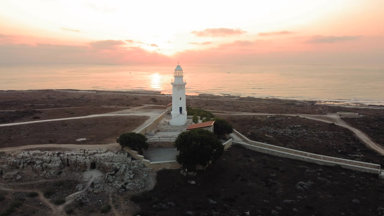 Veduta aerea di un faro bianco che si erge su un paesaggio costiero durante un tramonto sereno con