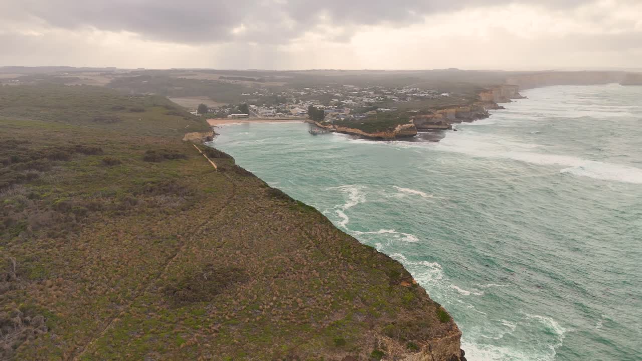 Drone footage captures the dramatic cliffs and ocean waves of Port Campbell, Australia, under overcast skies with steady camera movement