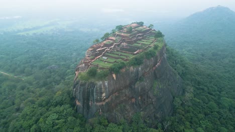 Filmische-Drohnenaufnahme-Von-Lions-Rock-In-Sri-Lanka-Mit-Nebligen-Bergen-Im-Hintergrund