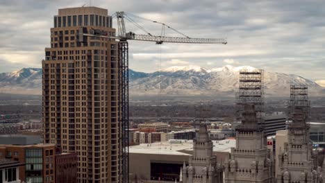 El-Centro-De-Salt-Lake-City,-Utah-Time-Lapse-Con-Una-Grúa-Moviéndose-En-Primer-Plano,-El-Templo-Mormón-Y-Las-Montañas-Y-Un-Paisaje-Nublado-En-El-Fondo