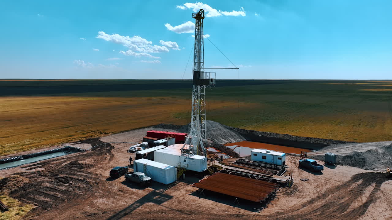 White metal derrick in the center of drilling site. Industrial production of oil or gas in the deserted area.