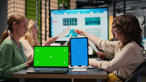 businesswomen working side by side with a green screen on the table