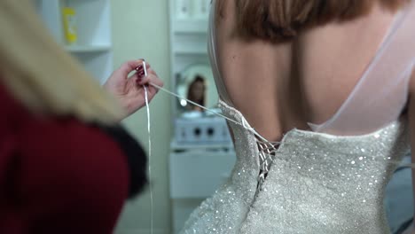 friend helps the bride to put on a wedding dress