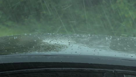 View-of-heavy-storm-hail-and-rain-falling-on-a-black-car,-nature-disaster,-climate-changes,-global-warming,-hot-summer-day,-medium-closeup-shot