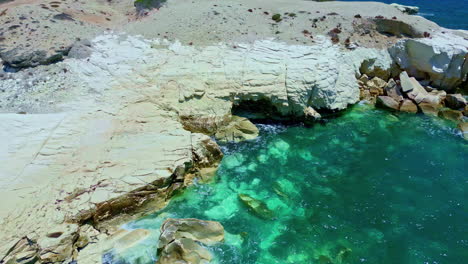 aerial drone zoom in shot over ocean waves crashing on the rocky island coast on a sunny day