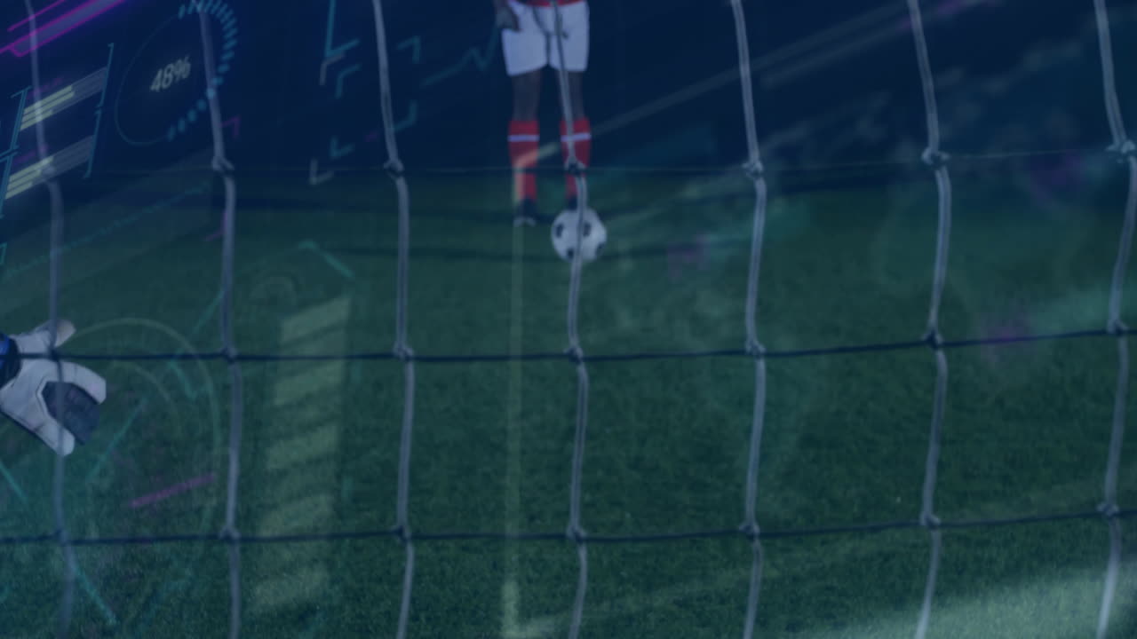 Pemain sepak bola berdiri di belakang gawang, menampilkan overlay analitik performa teknologi di lapangan pada malam hari.