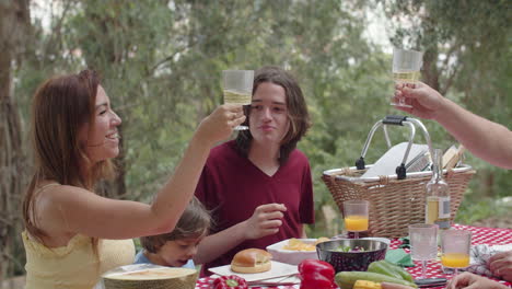 Caucasian-parents-and-kids-sitting-at-table-in-nature-and-eating