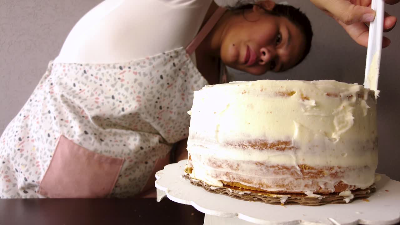 mujer latina con un delantal preparando la cocina horneando un pastel esparciendo glaseado de mantequilla con una espátula de pastel de plástico blanco