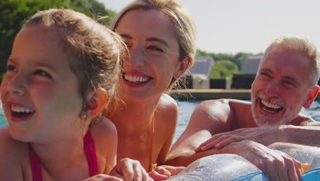 smiling multi-generation family on summer holiday relaxing in swimming pool on airbed