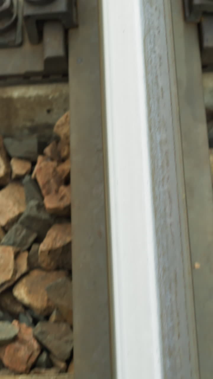 철도 트랙의 고정 시스템의 클로즈업 뷰, 비디오는 비석 돌로 둘러싸인 콘크리트 슬리퍼에 철도를 고정시키는 볼트와 견과류를 강조합니다.