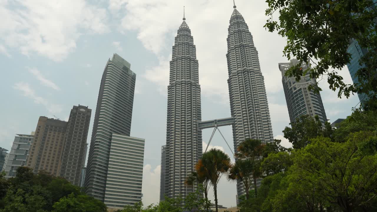 Vegetación tropical enmarcando las Torres Petronas en Kuala Lumpur, día soleado.