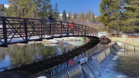 video footage of two skiers walking across a bridge that is over a small waterfall