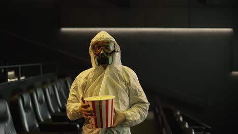 a man in white protection costume and respirator came alone to the cinema with bucket of popcorn, slow motion