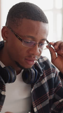 student in glasses uses computer in library. african american man with earphones takes off glasses looking attentively at screen. exams preparation at university