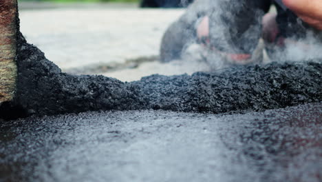 road construction workers manually spread and adjust hot tar or asphalt on the ground at the pavement building site