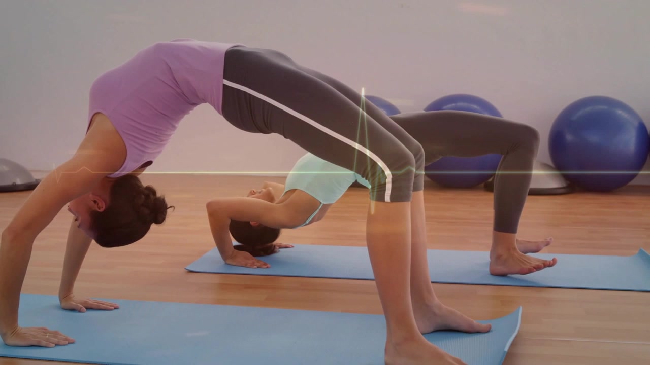Two women on cue, lifting into bridge for fitness on blue mats, ECG overlaying torsos