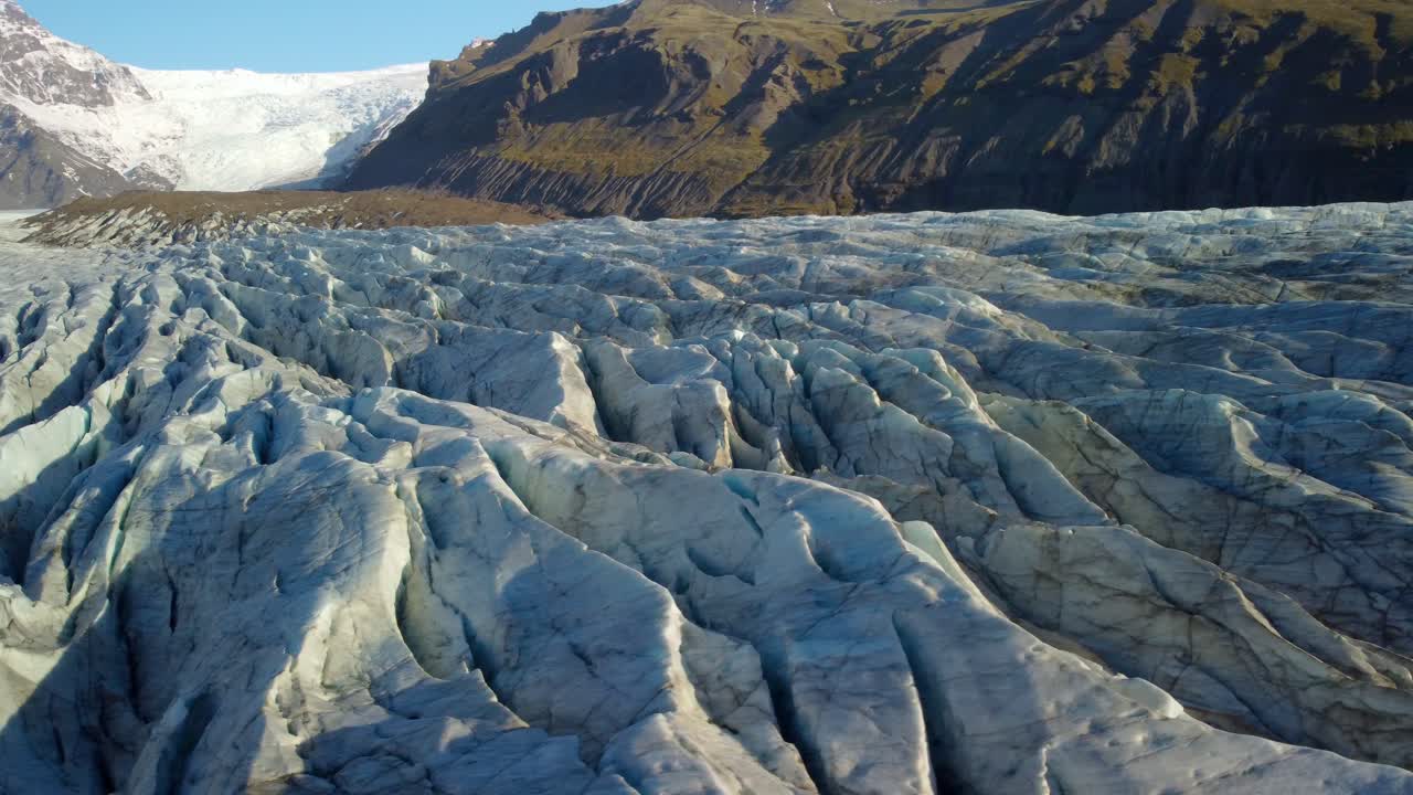 vista aérea sobre una textura glaciar helada, hacia una montaña iluminada por el sol en islandia