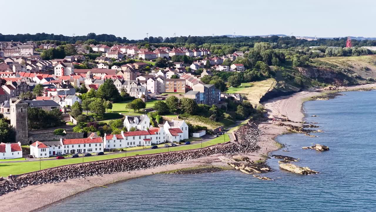 Drönare glider ovanför kuststaden Fife och avslöjar strandhus, ett historiskt torn och en kuperad kustlinje