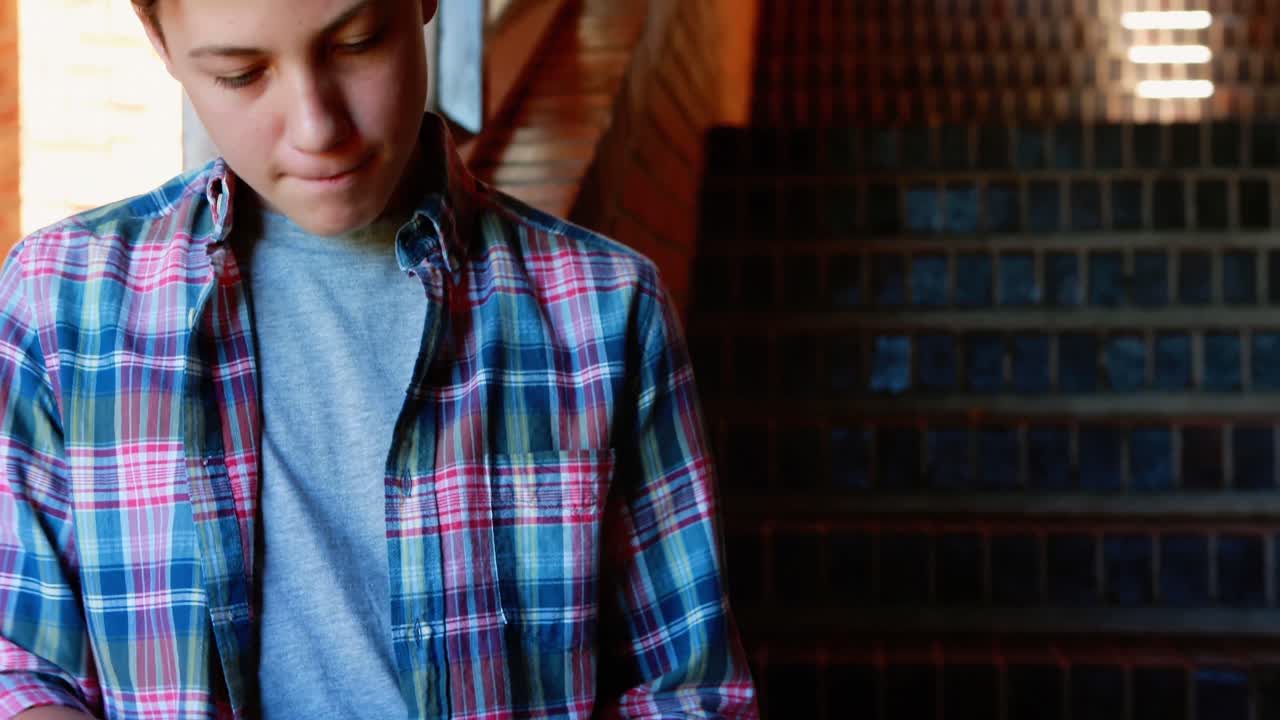 escolar sonriente usando una tableta digital cerca de la escalera