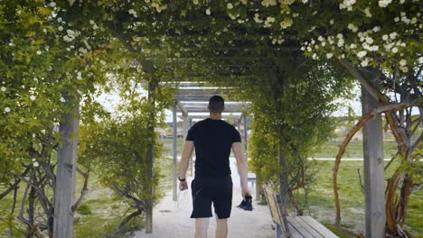 panning shot of an athletic man walking through a floral archway holding gym equipment