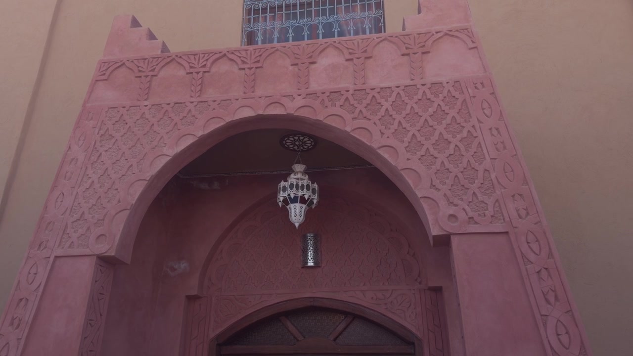 Arco marocchino in gesso intagliato e decorato con lanterna sospesa e motivi a rilievo geometrici.
