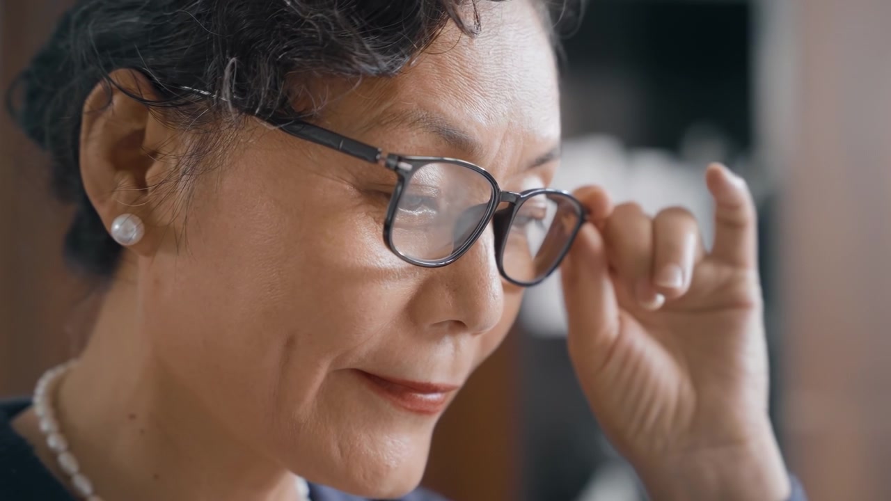 Donna anziana in pensione con presbiopia e vista debole, che indossa occhiali e cerca di leggere un libro, un giornale o le notizie. La donna soffre di ipermetropia, una patologia oculare; la presbiopia è caratterizzata da sintomi specifici, richiede diagnosi e trattamento