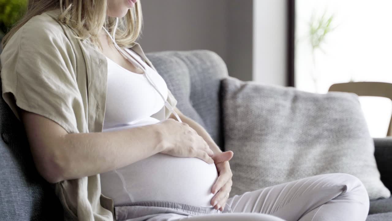 спокойная беременная женщина наслаждается музыкой и массирует живот