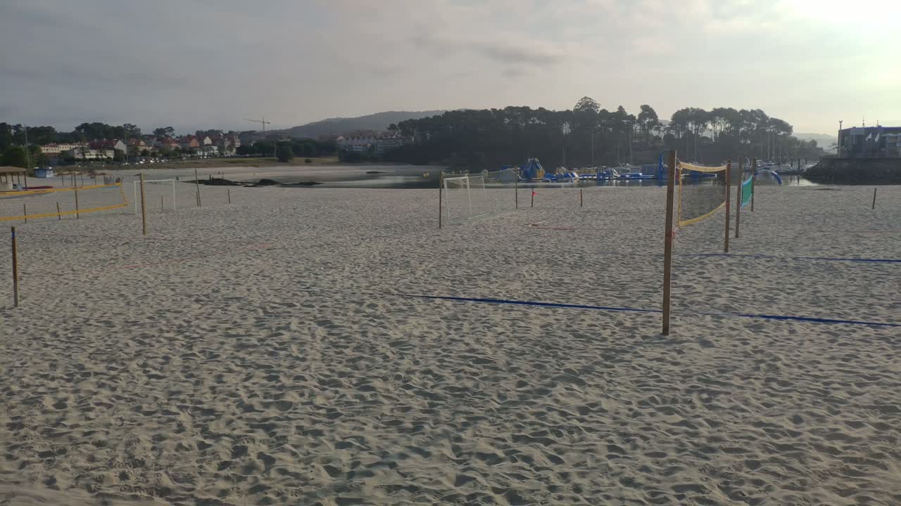 zona de playa con campo de fútbol en la arena y voleibol sin gente en una mañana nublada a principios de verano, rodando a la derecha