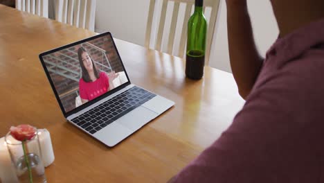 Mixed-race-man-sitting-at-table-using-laptop-making-video-call-with-female-friend