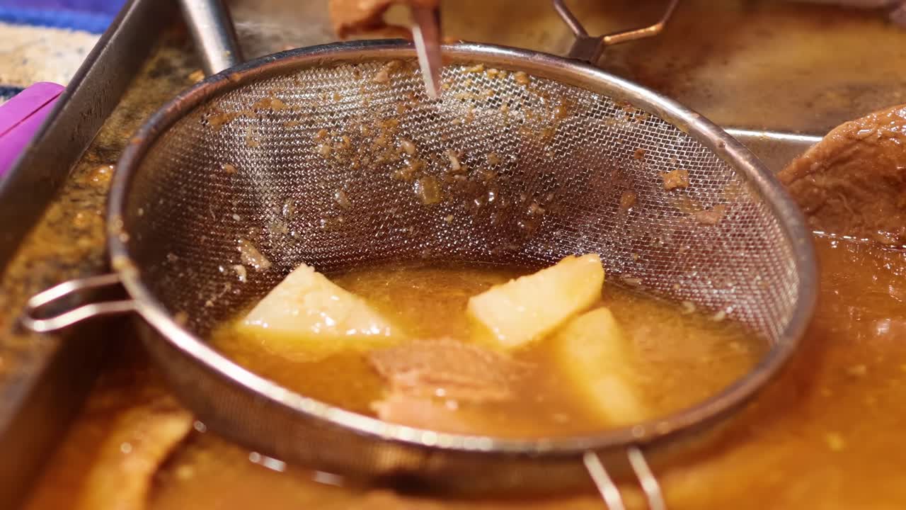 Close-up of offal being sifted and cooked in a flavorful broth using a metal sieve.