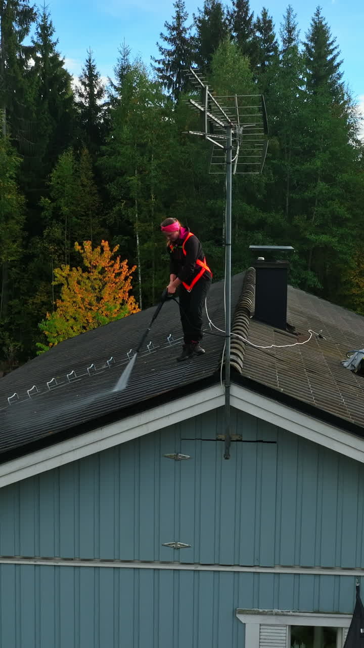 Vertical drone shot in front of a woman pressure washing a house roof, fall day