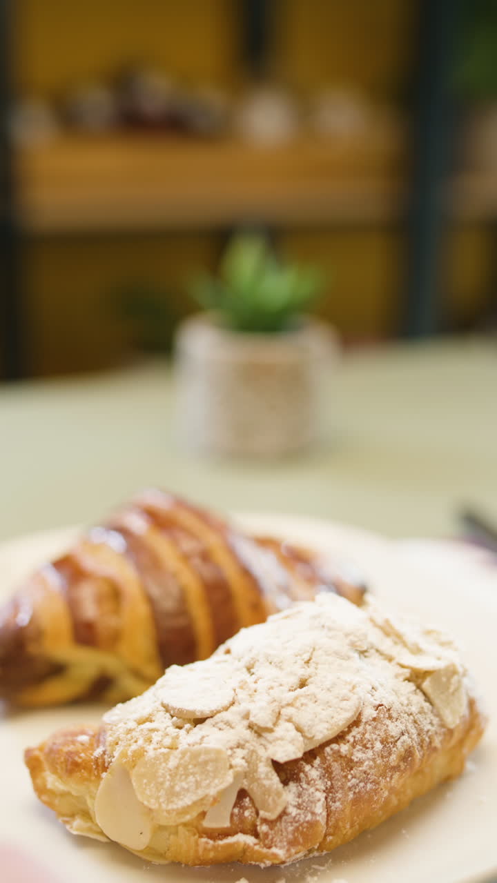 Close-up of a sweet croissant glazed and sprinkled with icing sugar, while a fork cuts a portion showing its crispy and soft texture