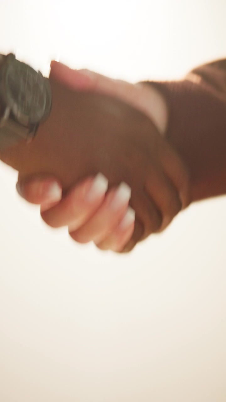 Nærbillede af to personer, der giver hånd, mod en lys baggrund