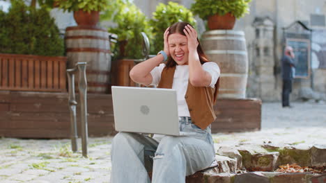 overjoyed happy young woman working on laptop celebrating win good message news in city street