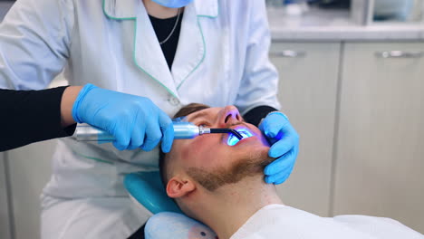 unrecognized female medic in white robe holding uv lamp in the male patient's mouth. future dentist's practice.