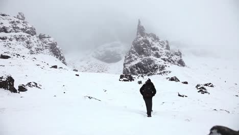 Adventurer-couple-walking-through-rocky-mountains,-winter-landscape,-snowy,-highlands,-Scotland,-static-shot,-low-angle