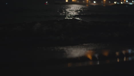 las olas oscuras del mar bañan la orilla con el reflejo de las luces por la noche.