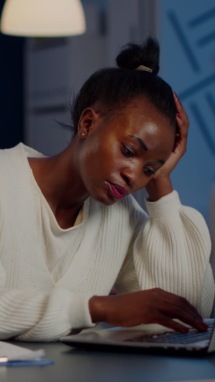 Vertical video Exhausted african freelancer resting head on hand in front of laptop working