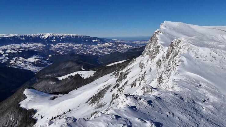 Cime innevate di Piatra Craiului viste dai Monti Bucegi sotto un cielo azzurro e limpido, vista aerea