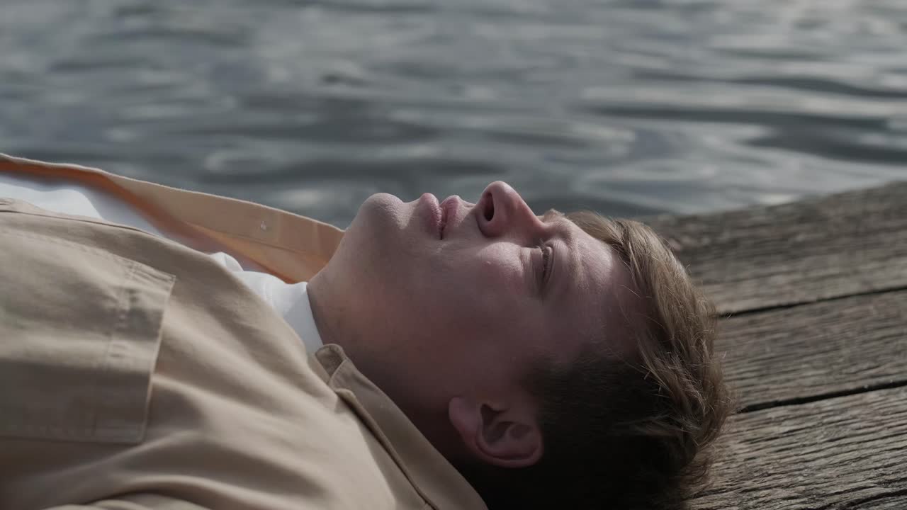 젊은이가 나무로 된 보행자 다리 위에 혼자 누워서 호수를 쳐다보고, 삶에 대해 생각하고, 자연에서 평화로운 분위기를 누리고, 신선한 공기를 즐기고, 뒤를 바라보고 있습니다.