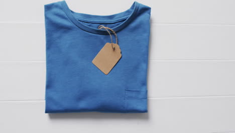video of flat lay of blue t shirt with tag and copy space on white background