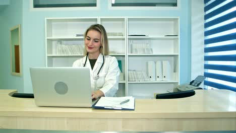 smiling medical nurse working on laptop and making notes at reception desk