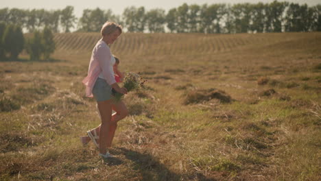 mother and daughter walking together in vast farmland under sunny sky with mother holding fresh flower bouquet in her right hand, surrounded by open field and distant trees