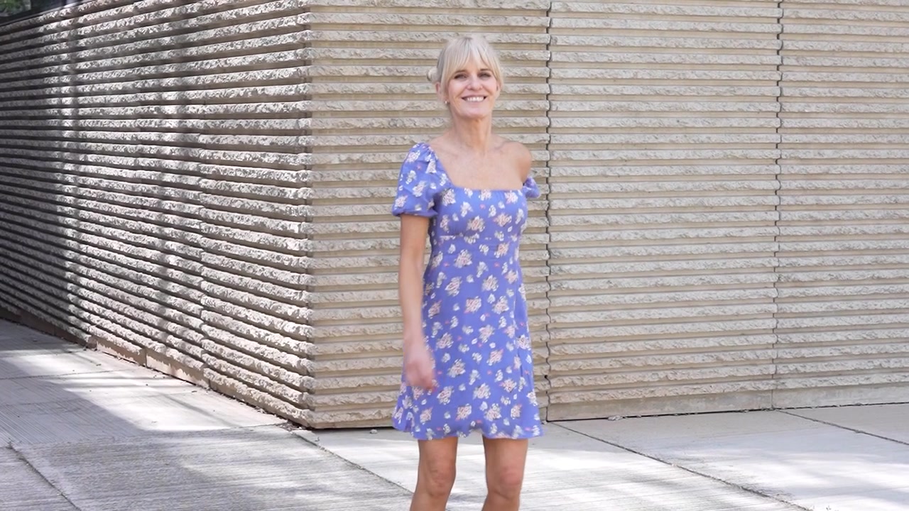 Uma mulher feliz, em um vestido azul, dança ao ar livre com uma atitude despreocupada em um dia ensolarado.