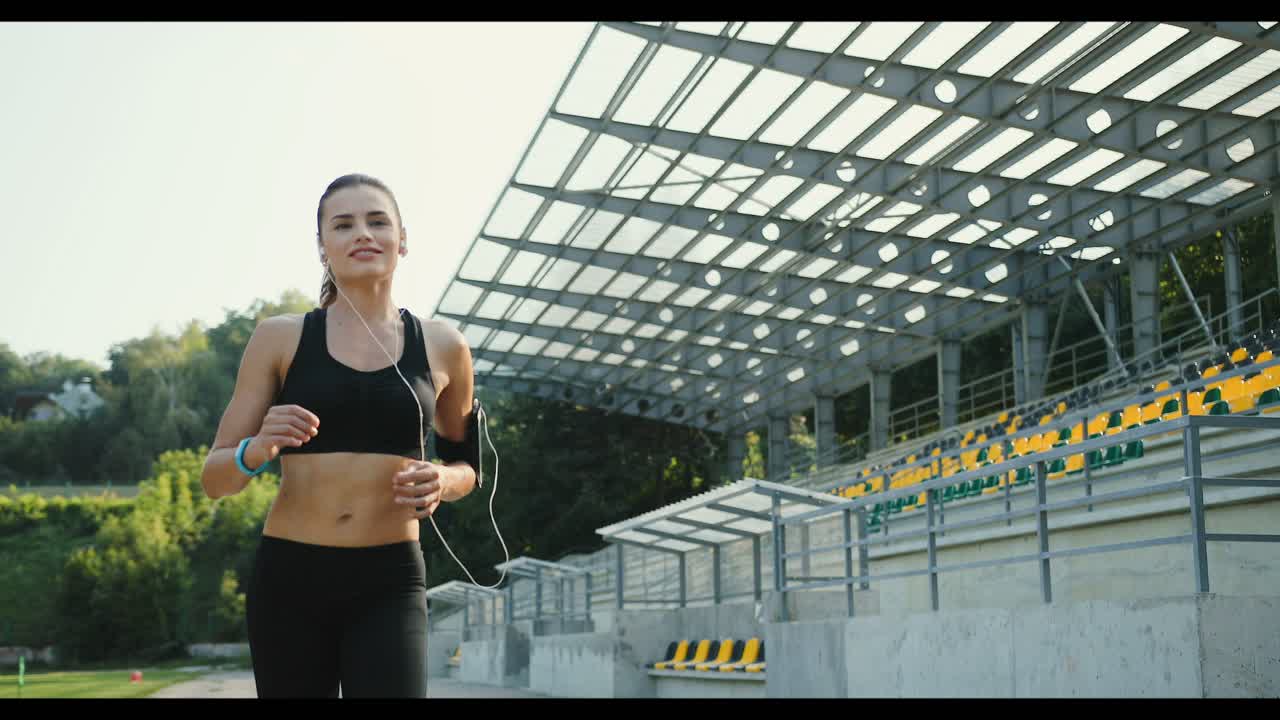 joven corredora escuchando música con auriculares mientras trotaba en el estadio en un día de verano