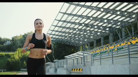 Junge-Joggerin,-Die-An-Einem-Sommertag-Beim-Joggen-Im-Stadion-Musik-Mit-Kopfhörern-Hört