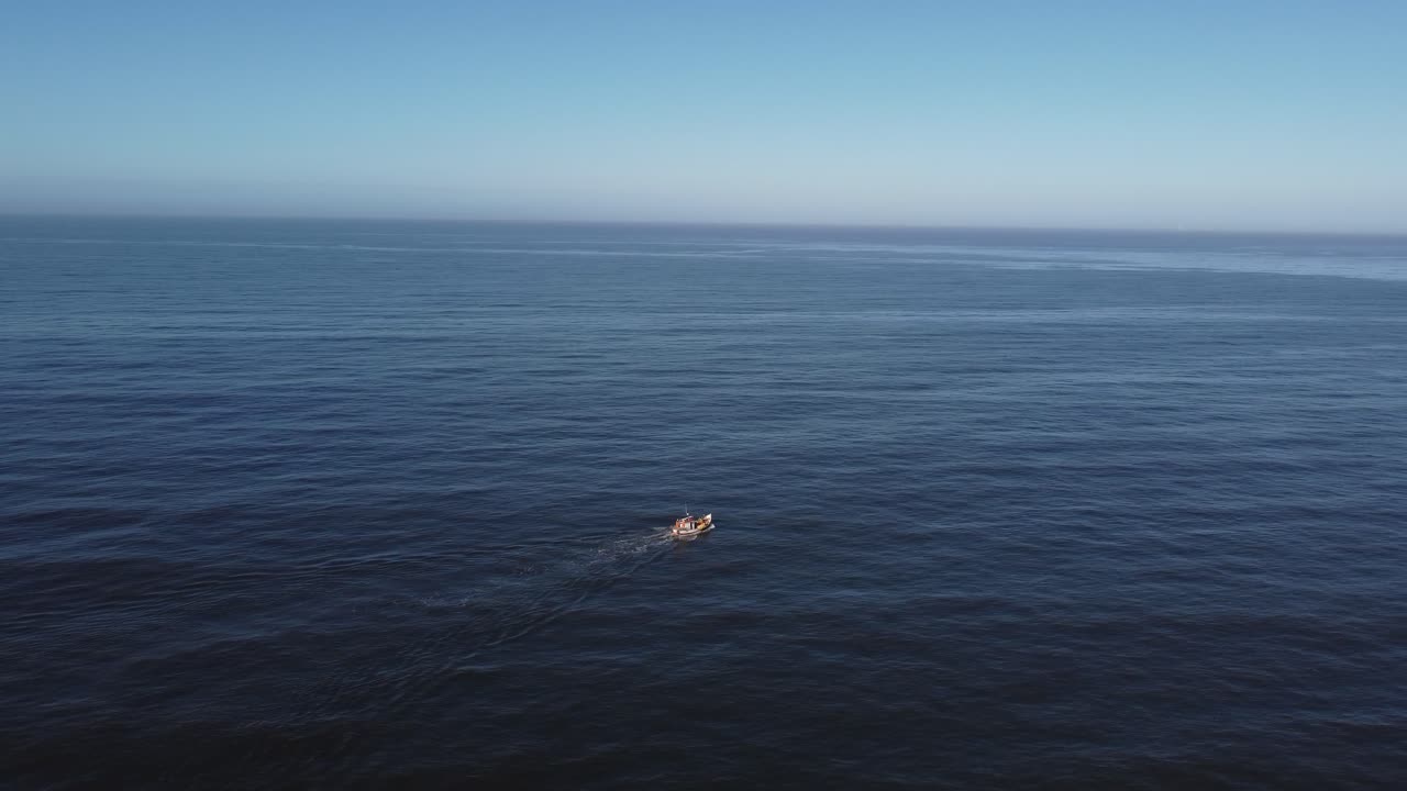 거대한 바다에서 항해하는 작은 흰색 보트의 공중 전망, 해안에서 점점 더 멀어짐